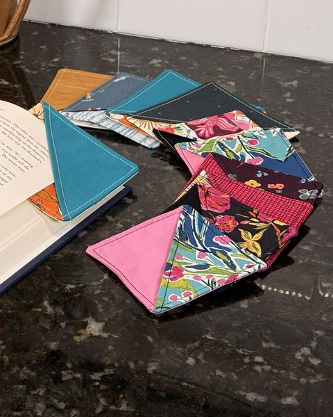 Fabric corner bookmarks in a fan of bright prints, one tucked on the corner of an open book