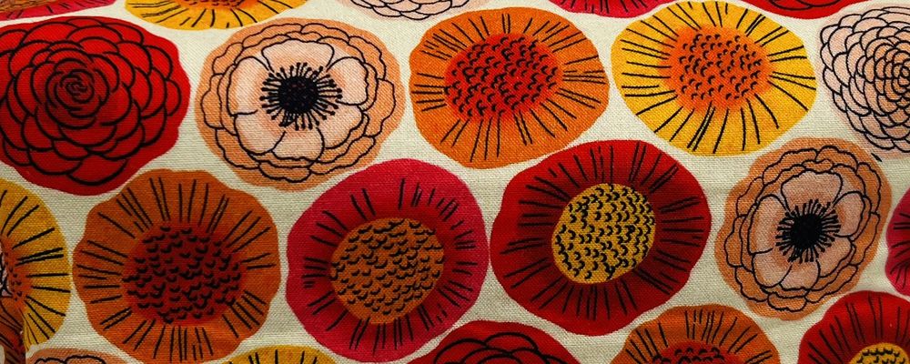Close-up of a cream fabric printed with red, orange and gold flowers